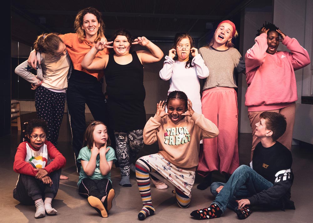 Gruppe von Quertanz-Tänzer*innen im Tanzraum des Esche Jugenkunsthauses. Die Kinder und Tanzpädagoginnen lächeln und machen coole Gesten. Fotografin: Katja Nitsche
